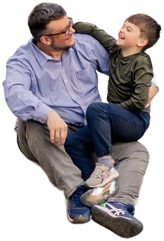 A dad and his young son laughing together, sitting on a rock in a creek