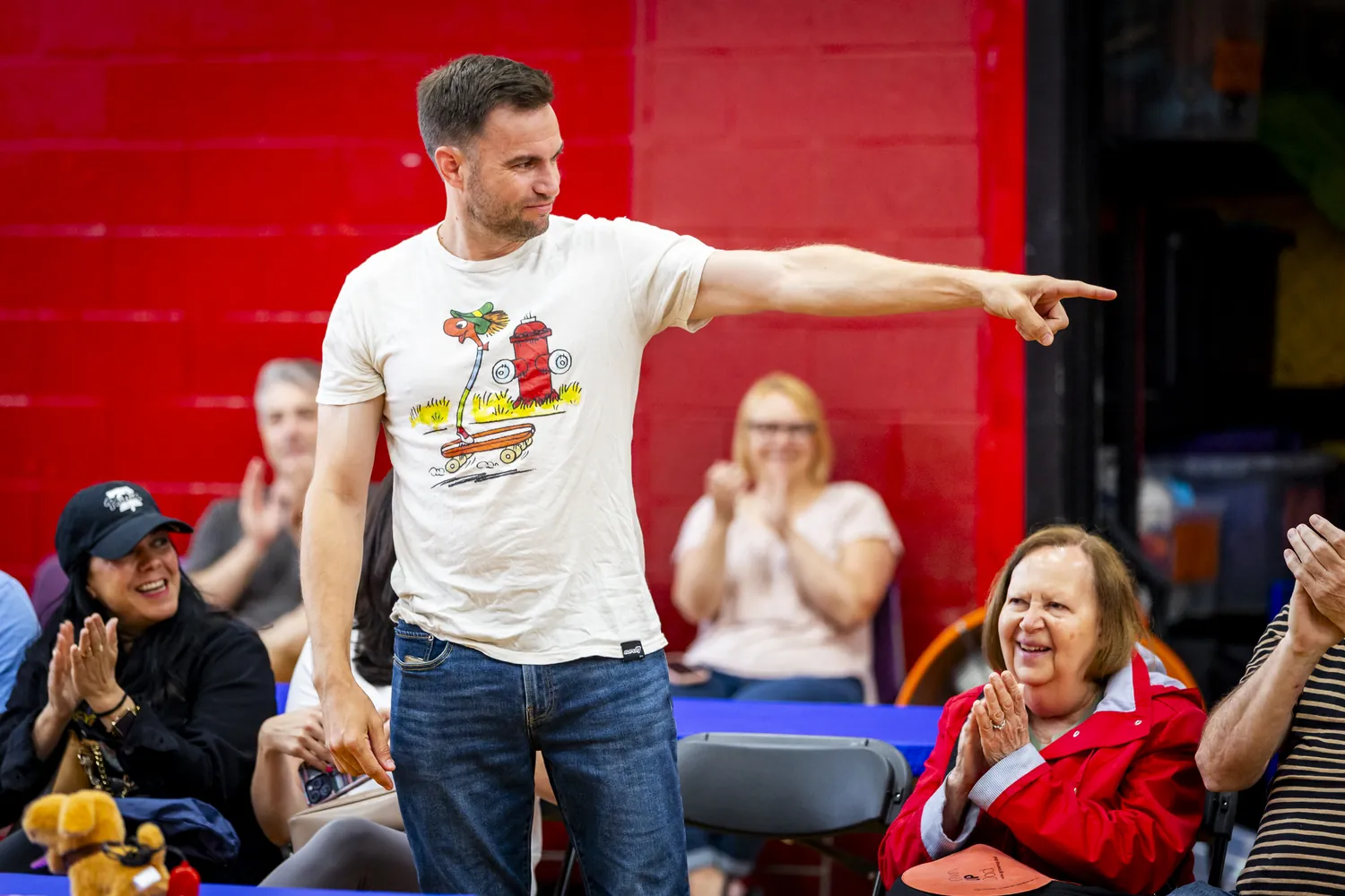 A dad pointing across the gym as the crowd laughs and claps